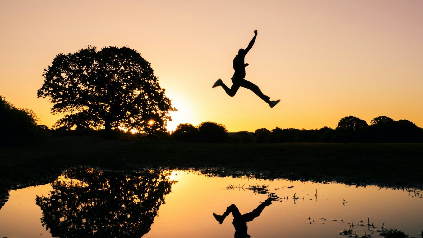 silhouette photo of man jumping on body of water during golden hour