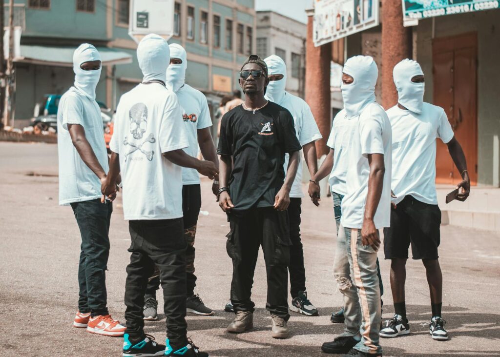 Group of Men in White T-Shirts and Balaclavas Standing on a Street