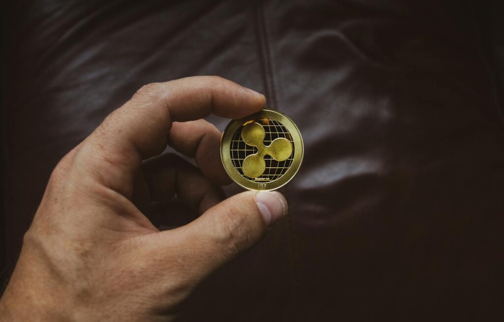 A close-up of a hand holding a gold Ripple cryptocurrency coin, symbolizing digital currency concept.