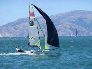 Dynamic sailboat race on a sunny day in San Francisco Bay against a mountainous backdrop.