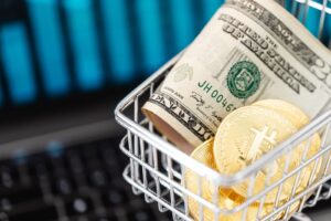 Close-up of bitcoin coins and US dollars in a shopping cart on a laptop, symbolizing digital finance.