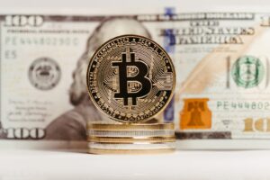 Bitcoin coin stacked with US $100 bill background, representing finance and cryptocurrency convergence.