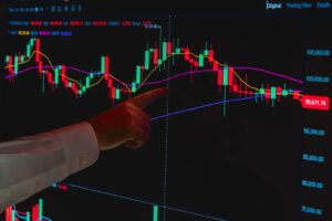 Hand pointing at stock market graph on a digital screen, symbolizing financial analysis.