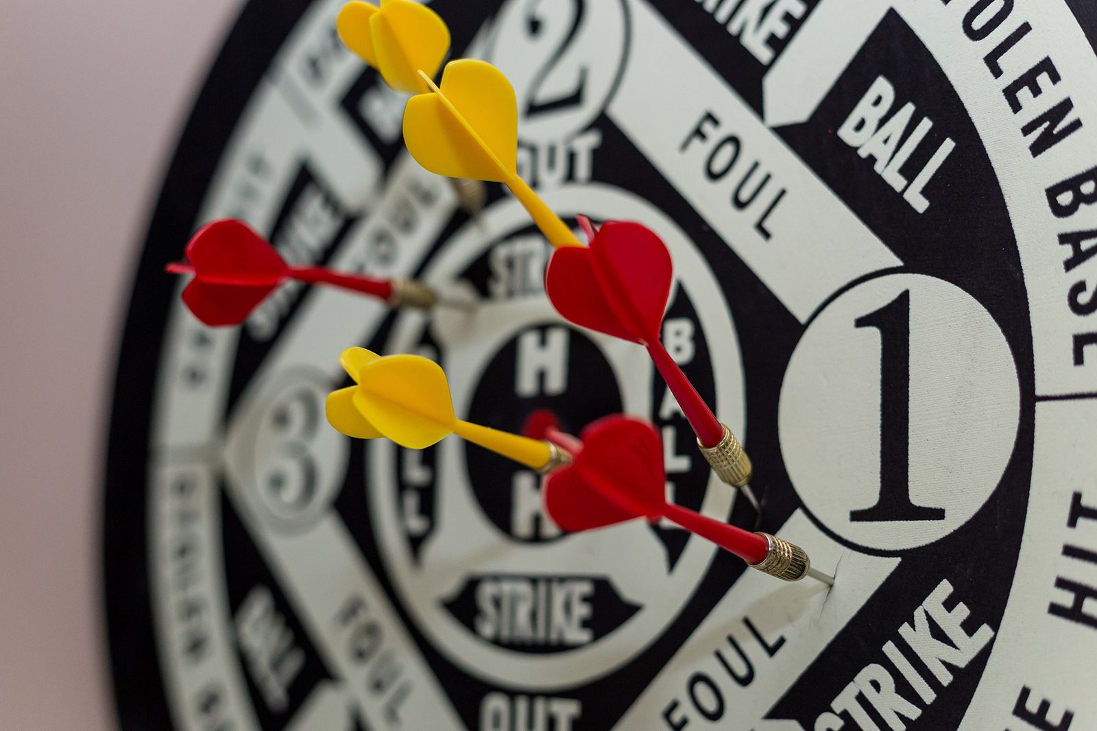 Vibrant close-up of yellow and red darts hitting the center of a dartboard indoors.