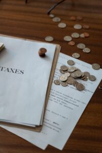 Close-up of tax documents and scattered coins on a wooden desk, representing finance and taxation.