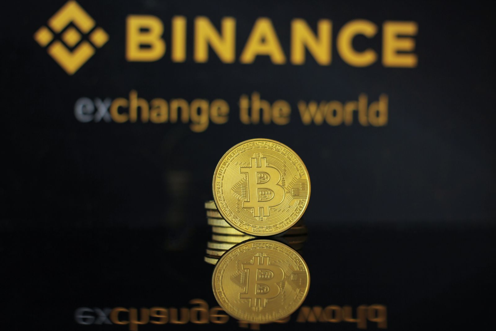 Close-up of a Bitcoin coin with Binance logo and text reflecting in dark surface.