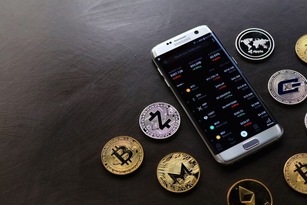 A collection of cryptocurrency coins and a smartphone displaying a digital trading platform.