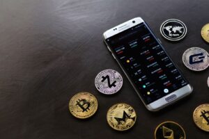 A collection of cryptocurrency coins and a smartphone displaying a digital trading platform.