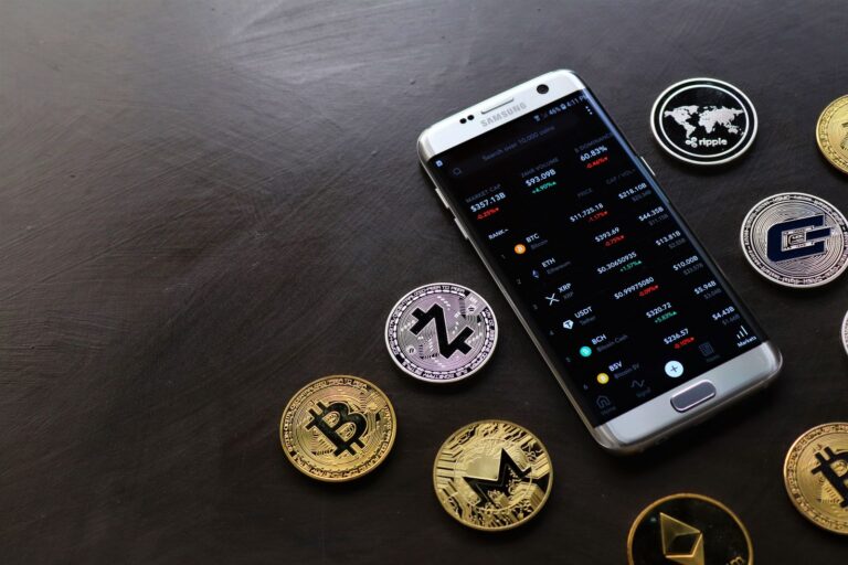 A collection of cryptocurrency coins and a smartphone displaying a digital trading platform.