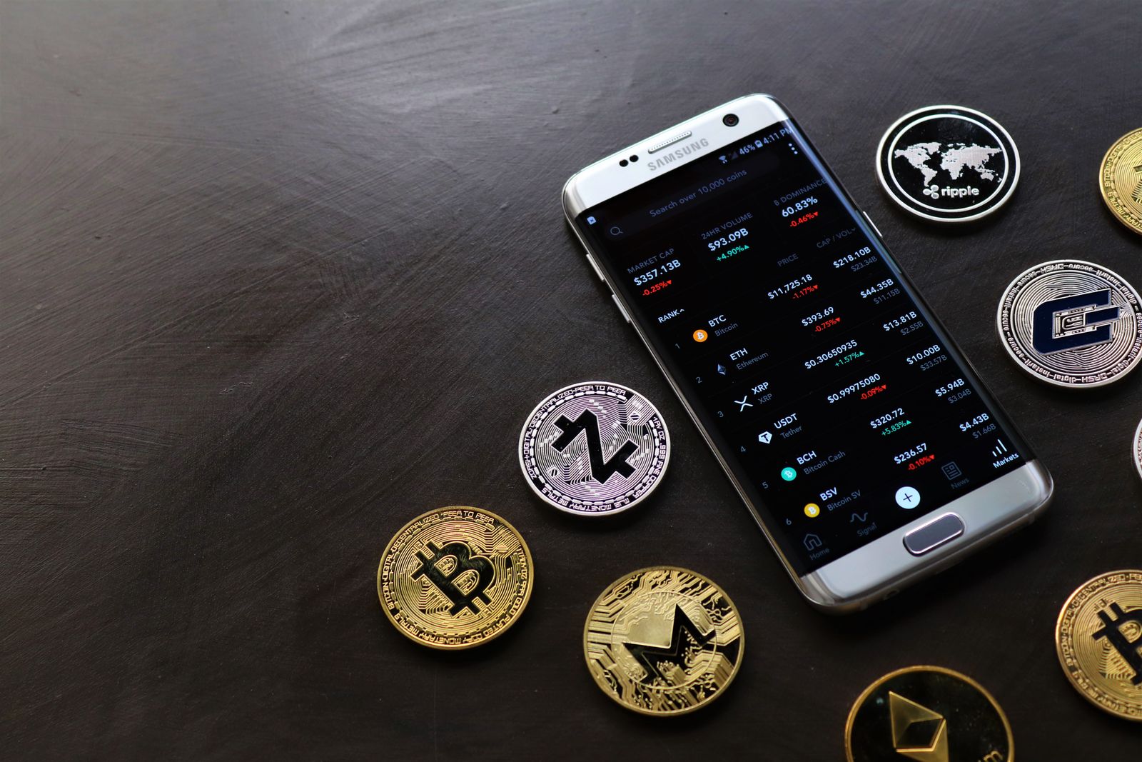 A collection of cryptocurrency coins and a smartphone displaying a digital trading platform.