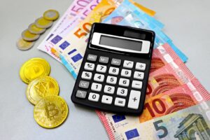 Calculator with euro banknotes and cryptocurrency coins like Bitcoin on a table.