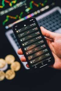 Hand holding phone showing cryptocurrency trends with coins in the background.
