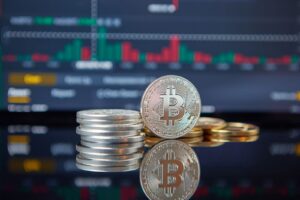 Stack of Bitcoin coins in front of a stock market graph, reflecting cryptocurrency trends.