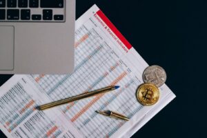 Top view of bitcoin coins on financial documents beside a laptop keyboard.