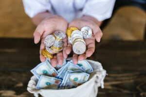 Person holding cryptocurrency coins above a bag of cash, symbolizing digital and traditional finance intersections.
