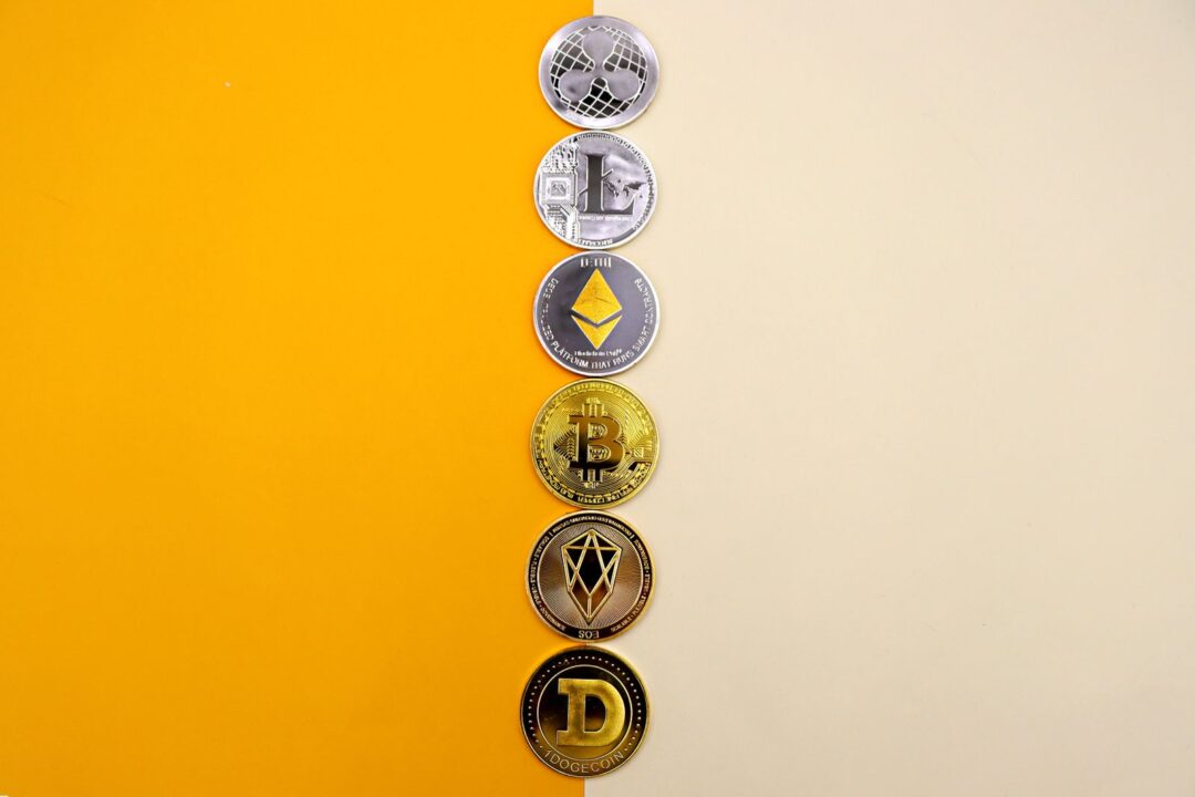 A row of cryptocurrency coins including Bitcoin, Ethereum, and Dogecoin on a vibrant yellow surface.