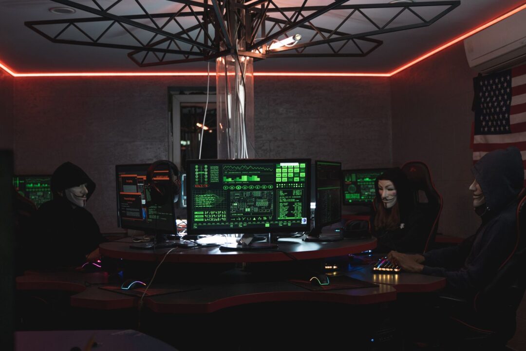 Team of hackers with Guy Fawkes masks coding in a dark room with computers.