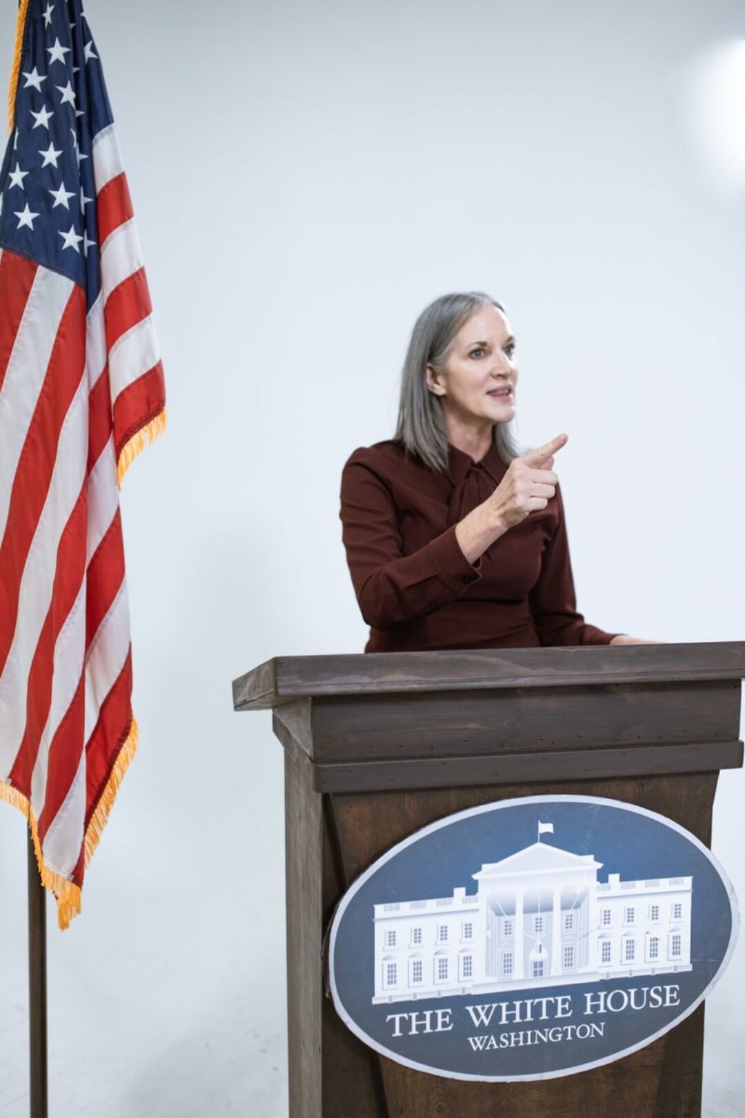 A woman speaks confidently at a podium with the American flag and White House insignia.