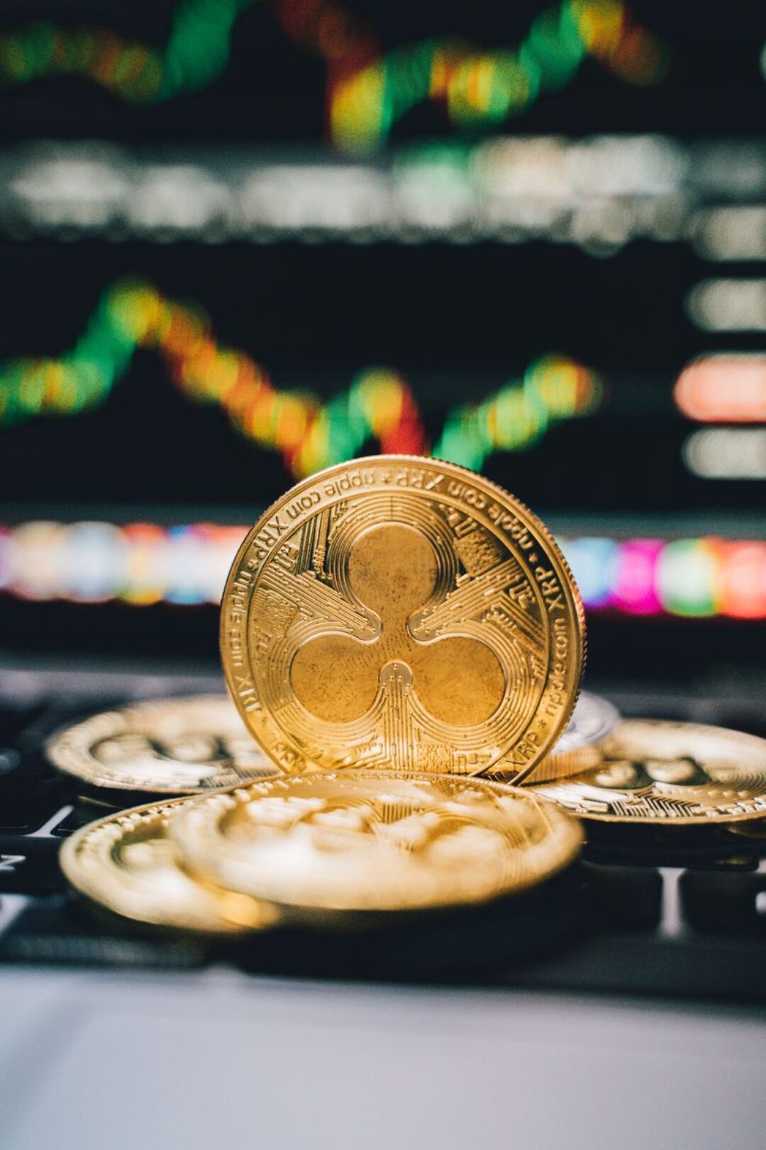 Gold Ripple coins on a laptop with a financial chart background, symbolizing digital currency trends.