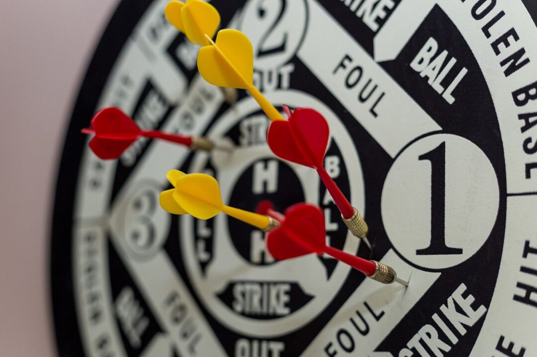 Vibrant close-up of yellow and red darts hitting the center of a dartboard indoors.