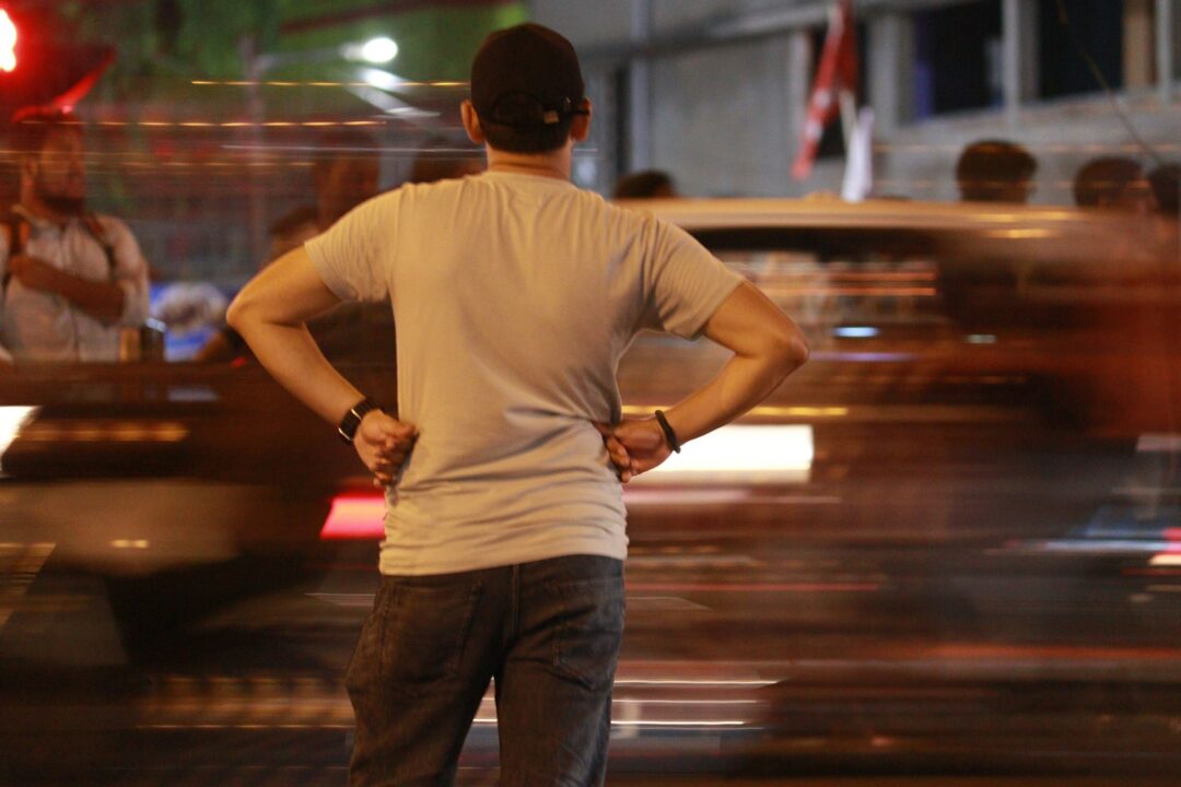 A man standing on a street corner with his hands on his hips